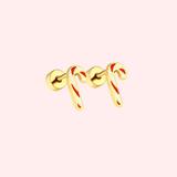 Gold candy cane-shaped earrings with red stripes on a light pink background