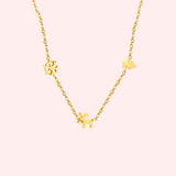 Gold necklace with Christmas charms on a light pink background.
