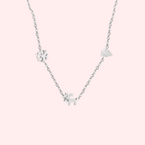 Silver necklace with Christmas charms on a light pink background.