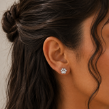 A close-up of a woman's ear wearing a small silver stud earring with a cluster of clear stones, shown against dark brown hair and warm skin tones.