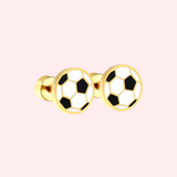 Gold football earrings on a pink background.