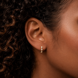 Close-up of model wearing Gold Bezeled Pear Huggie Earrings with clear pear-shaped cubic zirconia stones in bezel settings