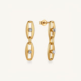 A pair of gold hoop earrings with elongated oval links and three clear round-cut gemstones, shown on a light cream background.