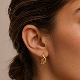 Close-up of model wearing Gold Wave Huggie Earrings with a curved twisted design that wraps closely around the earlobe