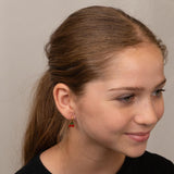 Close-up of a girl wearing a gold cherry earring against a neutral background