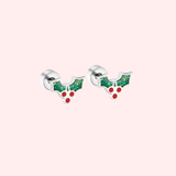Silver earrings with green holly leaves and red berries on a light pink background