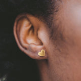 Close-up of an ear wearing a gold heart-shaped earring.