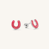 A pair of silver horseshoe stud earrings decorated with sparkling clear crystals along the red-pink enamel curve, shown on a clean off-white background.