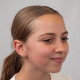 Girl with a ponytail wearing pink bow earrings against a plain background