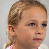 Close-up of a young girl wearing a flower-shaped earring against a neutral background