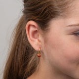 Close-up of a girl wearing a gold earring with a red flower against a neutral background