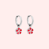 Silver hoop earrings with red flower charms on a light pink background