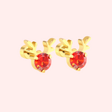 Gold Rudolph earrings with red gemstones on a light pink background.