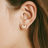 Gold butterfly earring worn by a girl with brown hair.