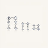 A set of silver-toned drop earrings with clear gemstones, shown in multiple sizes on a light cream background.