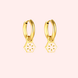 Gold hoop earrings with snowflake charms on a pink background.