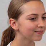 Close-up of a girl wearing bow earrings against a neutral background.