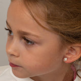 Close-up of a young girl wearing a cupcake earring against a neutral background