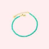 Turquoise beaded bracelet with gold clasp on a light pink background