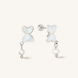 A pair of silver drop earrings featuring heart-shaped mother-of-pearl inlays and a dangling baroque pearl bead, shown on a light cream background.