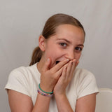Girl covering her mouth showing the bracelets against a plain background