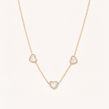 Gold necklace with heart-shaped pendants on a light beige background