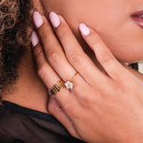 Close-up of a hand wearing two gold rings with a diamond, against a blurred background.