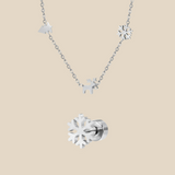 A silver Christmas charm necklace and a snowflake earring on a beige background.