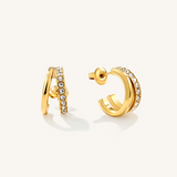 A pair of gold hoop earrings with rows of clear pavé-set gemstones, shown from side and back angles on a light cream background.