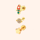 Three gold earrings with rocket, planet, and star designs on a light pink background