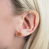 Close-up of a girl wearing a gold  pumpkin-shaped earring with blonde hair.