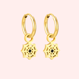 Gold hoop earrings with spider web charms on a light pink background