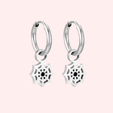 Silver hoop earrings with spider web charms on a light pink background