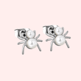Spider-shaped earrings with pearl centers on a light pink background