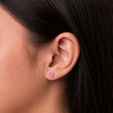 A close-up of a girl's ear wearing a small pink stud earring with a smiling face design.