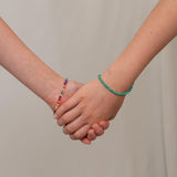 Two hands holding each other with colorful bracelets on a plain background