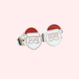 A pair of silver santa earrings on a light pink background.