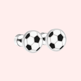 Silver football earrings on a pink background.