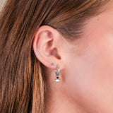 Close-up of a girl wearing silver hoop snowman earrings with a blurred background.