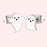A pair of silver stud earrings designed to resemble ghosts, displayed against a pink background.