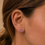 A close-up of a girl's ear wearing a small horse-shoe shaped stud earring set with pink stones.