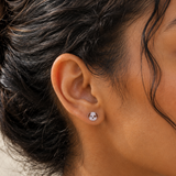 A close-up of a person's ear wearing a small stud earring shaped like a white dog face with brown ears and black details.