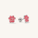 A pair of silver stud earrings shaped like pink paw prints, embellished with small clear rhinestones, shown on a light cream background.