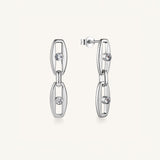 A pair of silver-toned geometric dangle earrings with open oval links and small clear gemstones, shown on a clean off-white background.