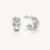 A pair of polished silver hoop earrings with a central channel set with clear round-cut gemstones, shown from both front and side angles on a light cream background.