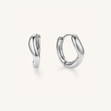 A pair of polished silver huggie hoop earrings with a smooth, organic wavy curve design, shown on a clean off-white background.
