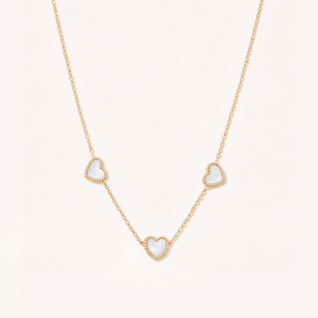 Gold necklace with heart-shaped pendants on a light beige background