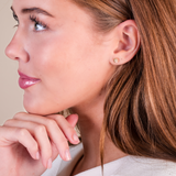 Close-up of a woman wearing a gold earring with a beige background