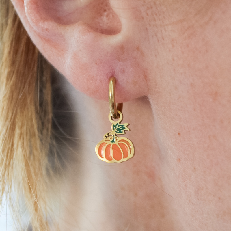 Gold earring with a pumpkin charm worn by a girl.