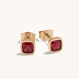 Gold earrings with red gemstones on a white background